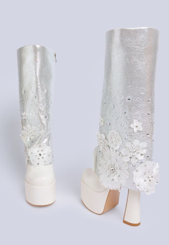 A rear view of two white 'Sundra' platform boots, highlighting the white glittery shaft, the zipper closure detail, the chunky block heels, and the intricate white floral appliques. Available from CO-Wear in Denver, Colorado USA.