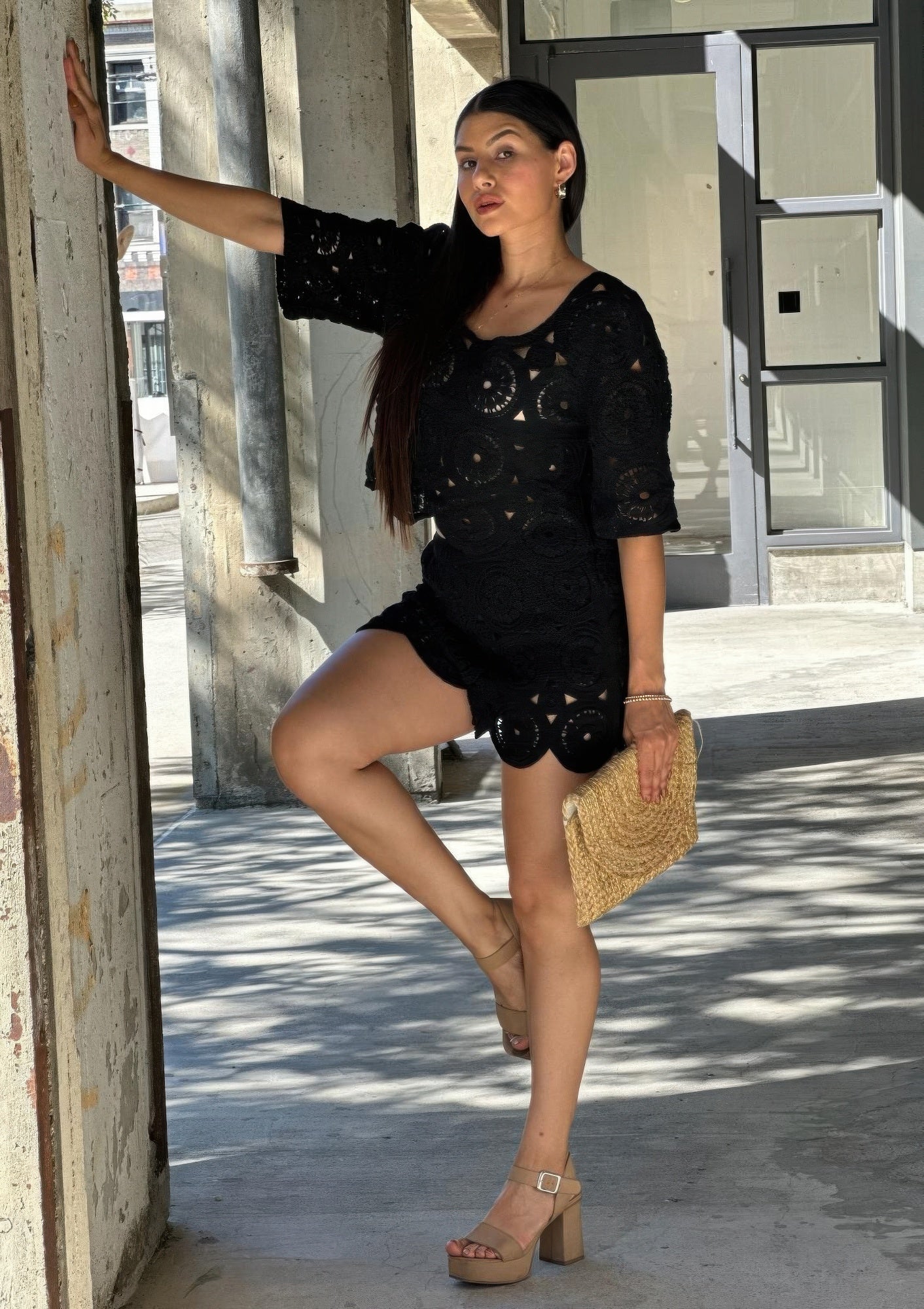 Model wearing a black crochet lace two-piece set, featuring a scoop-neck crop top and matching shorts with scalloped hems, holding a woven clutch. Denver, Colorado USA.