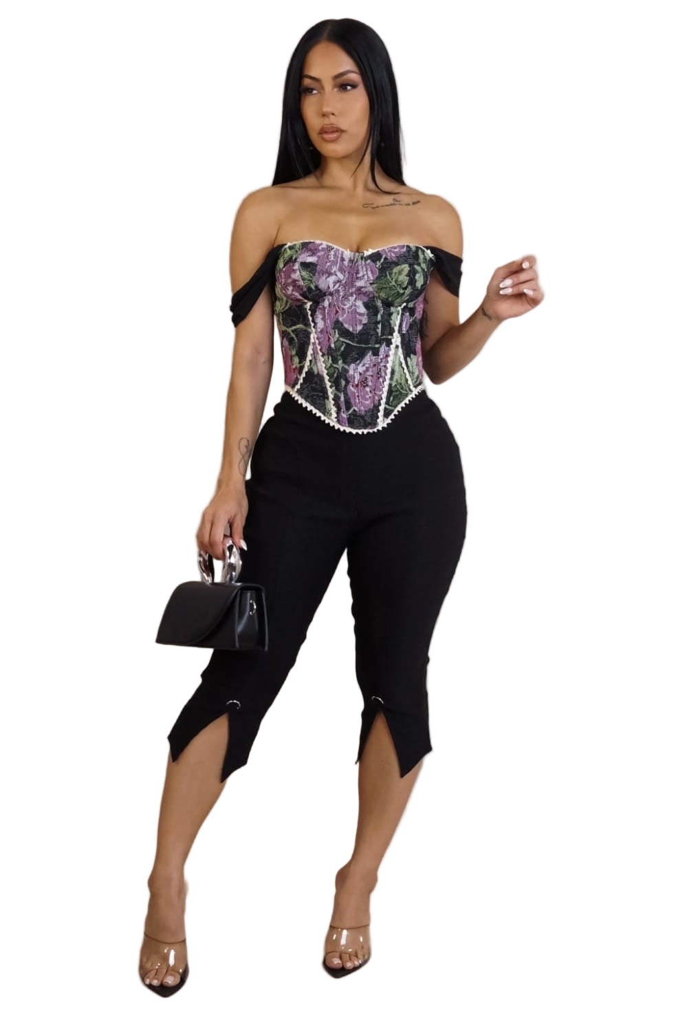 Woman wearing a floral corset top and black pants against a plain background