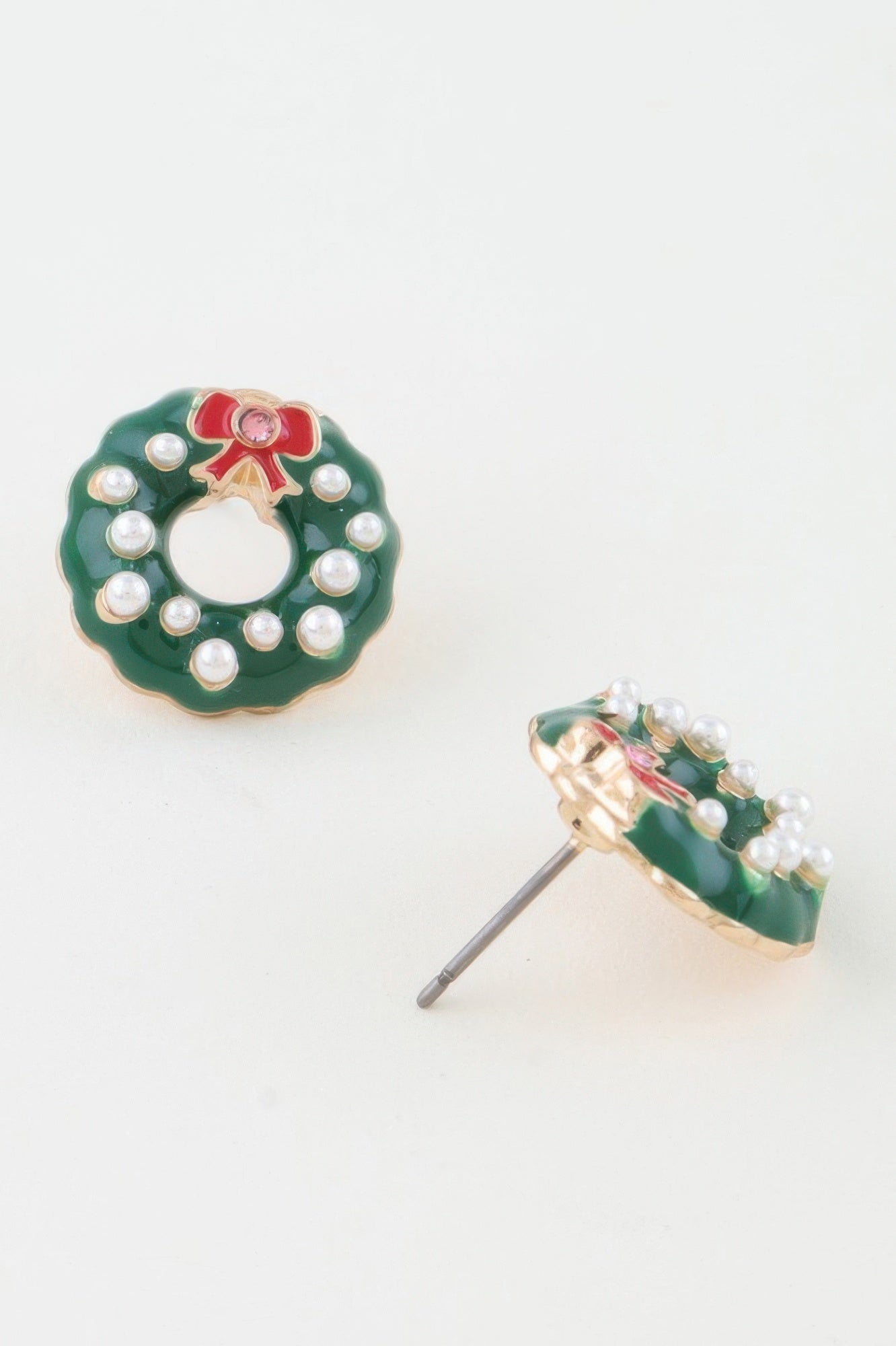 A pair of festive Christmas wreath stud earrings featuring green enamel, small faux pearls, a red bow, and a visible post backing. Available from CO-Wear in Denver, Colorado USA.