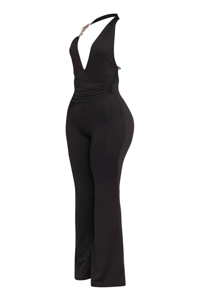 
                  
                    A full-length, slightly angled view of a black halter jumpsuit with a deep V-neckline and a gold-toned chain detail on the right strap. The jumpsuit features ruching at the waist and flared legs. It is displayed on a mannequin or stand against a white background.
                  
                