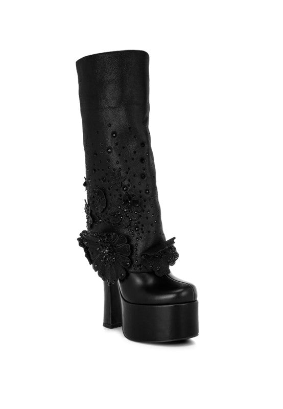 A front three-quarter view of the black 'Sundra' platform boot, featuring a thick platform sole, a chunky block heel, and the shaft adorned with subtle black floral appliques and bead embellishments. Available from CO-Wear in Denver, Colorado USA.