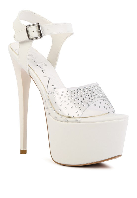 A front three-quarter angled view of the white 'First Date' sandal, showcasing the ultra-high stiletto heel, the massive white platform, and the clear toe strap studded with rhinestones. Available from CO-Wear in Denver, Colorado USA.