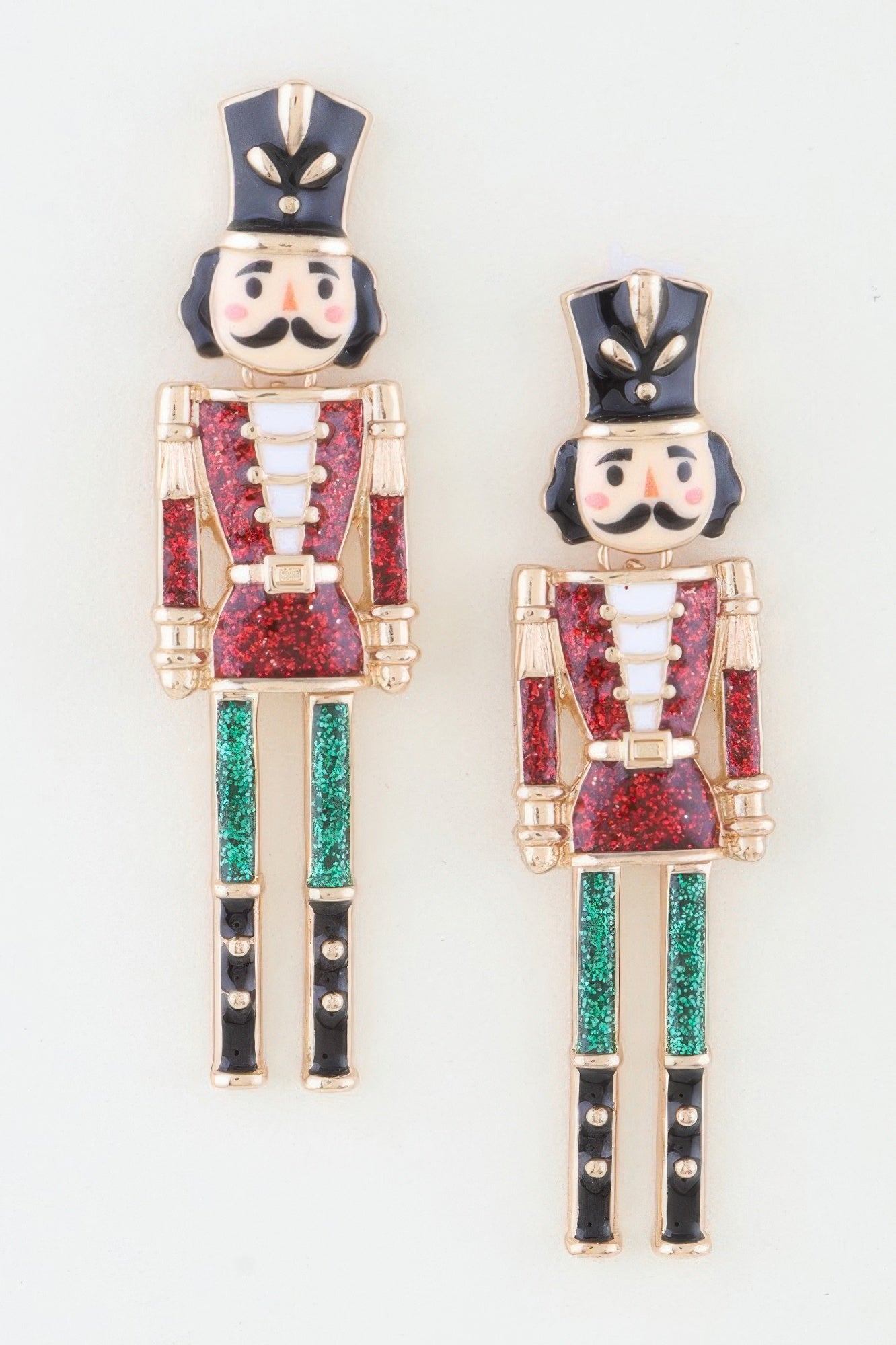 A pair of gold-toned dangle earrings shaped like nutcracker soldiers, featuring black, red glitter, and green glitter enamel detailing. Available from CO-Wear in Denver, Colorado USA.