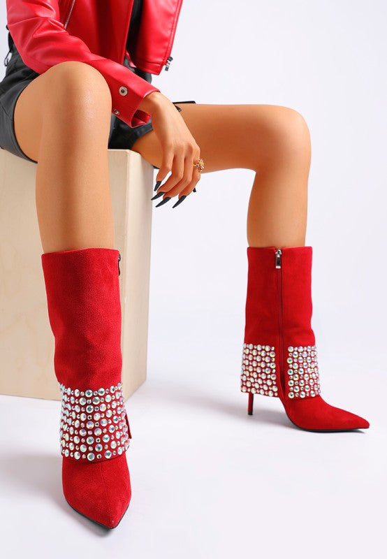 A model is sitting, wearing bright red suede stiletto boots that feature a wide fold-over cuff and rows of iridescent diamante studs around the ankle and heel. The boots have a pointed toe and a tall stiletto heel. Available from CO-Wear in Denver, Colorado USA.