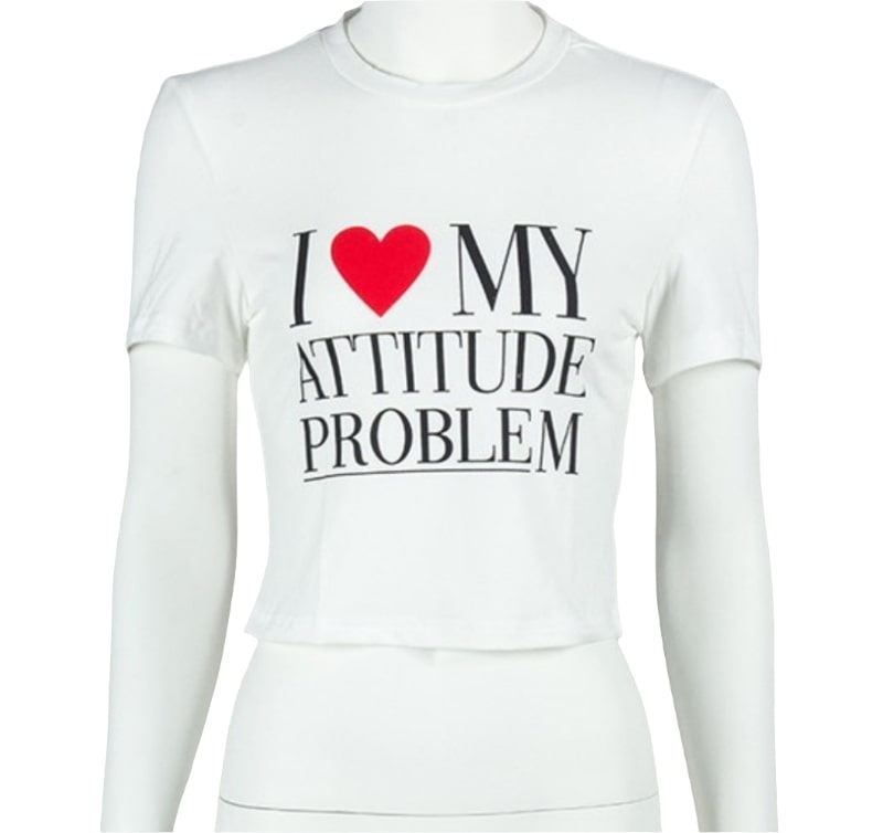 A white short-sleeve crop top is displayed on a mannequin. The front of the shirt features bold black text that reads "I ❤️ MY ATTITUDE PROBLEM" with a red heart icon replacing the word "love". The background is solid white.
