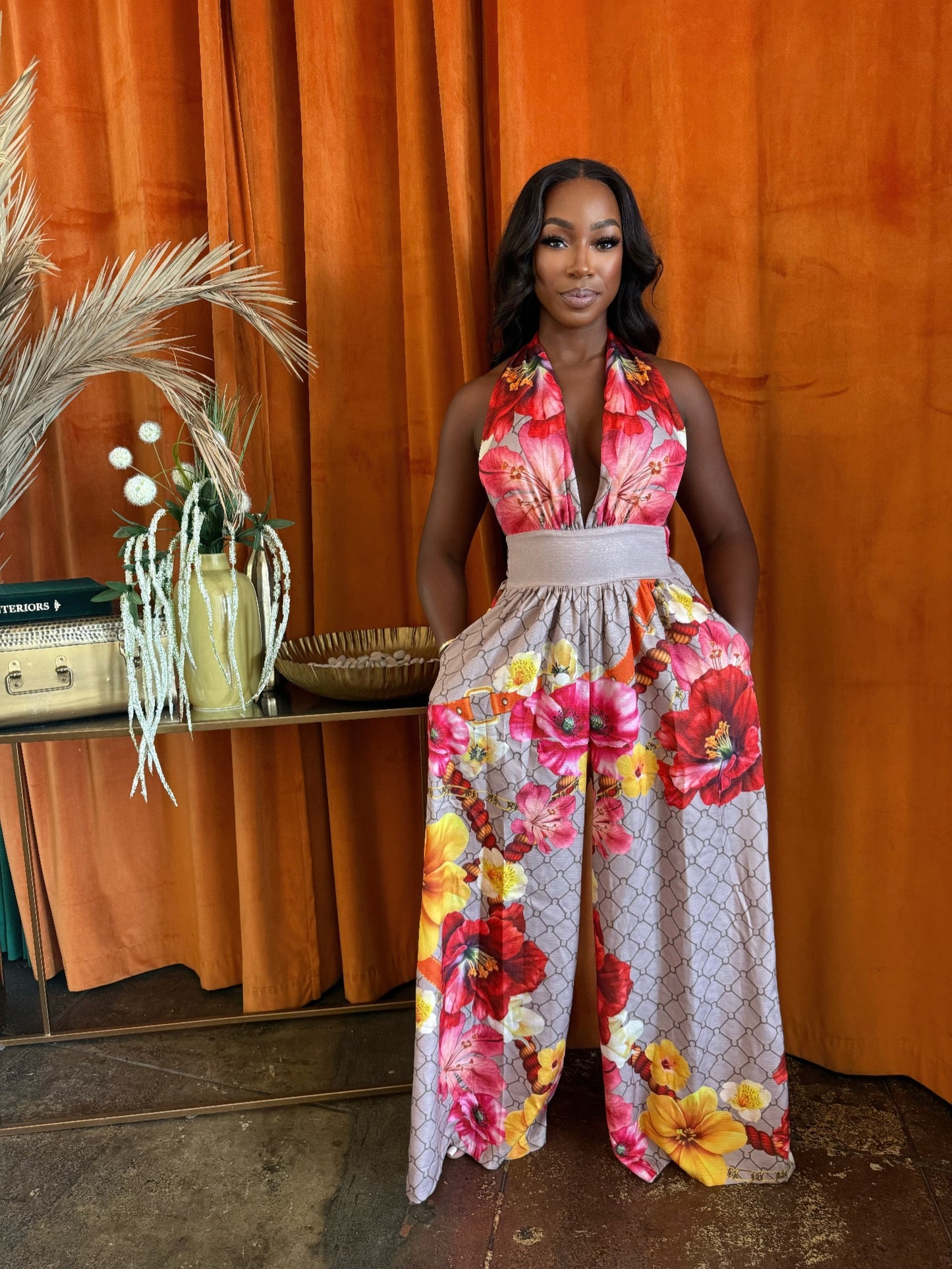 Model in the colorful Paradise Bloom Jumpsuit, featuring a halter neck, wide-leg pants with a large floral design, and a contrasting wide waistband. Denver, Colorado USA.