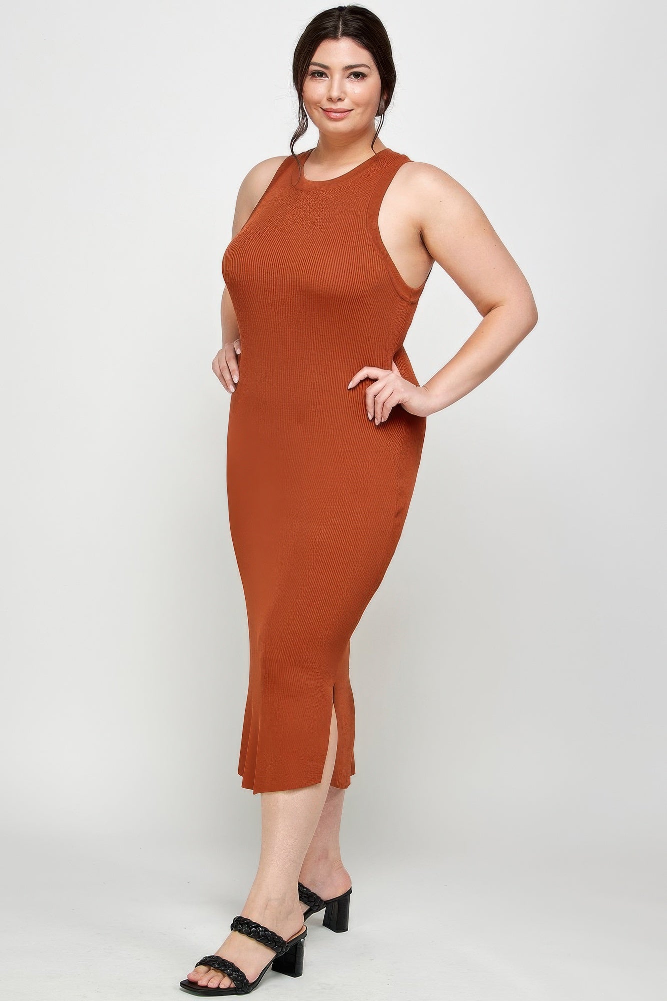 Side view of the model in a plus size, rust-colored stretchy ribbed midi dress with a racer back and a small vertical side slit. Denver, Colorado USA.