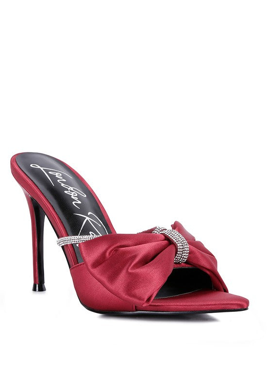 A side profile view of the striking red satin high-heeled sandal, showcasing the thin stiletto heel, the ruched satin bow secured by a rhinestone band, and the pointed toe. Available from CO-Wear in Denver, Colorado USA.