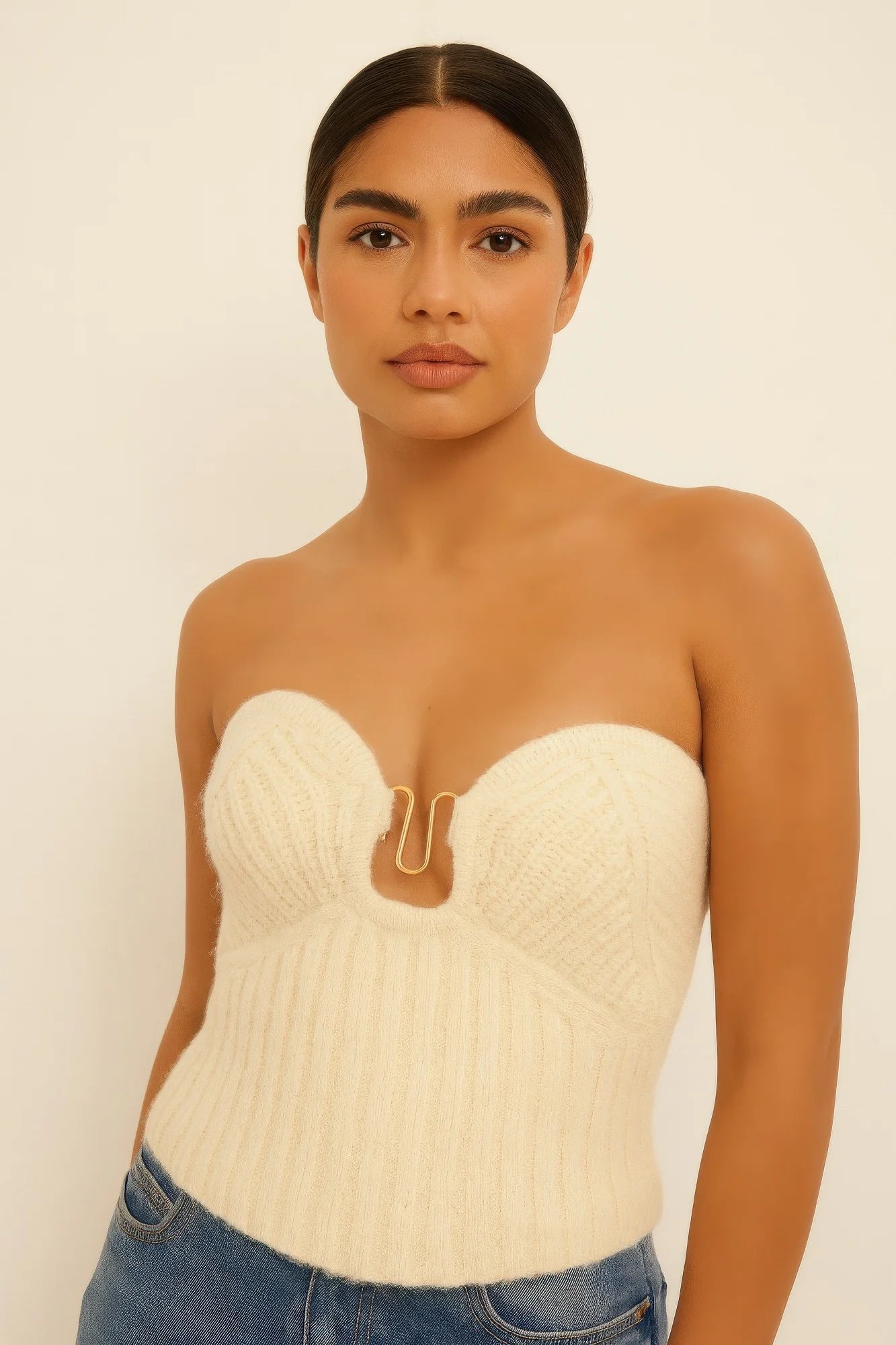 Close-up of a model wearing a cream strapless ribbed knit top with a sweetheart neckline and gold metal detail at the bust. Denver, Colorado USA.