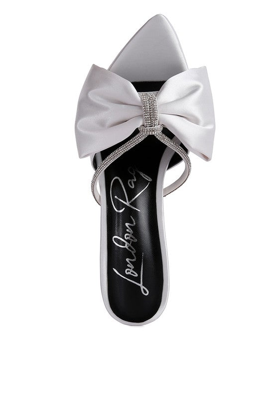 A top-down view of the white satin high-heeled sandal, featuring a wide, puffy bow centered with a silver rhinestone band and thin jewel straps across the footbed. The footbed has black cursive writing. Available from CO-Wear in Denver, Colorado USA.