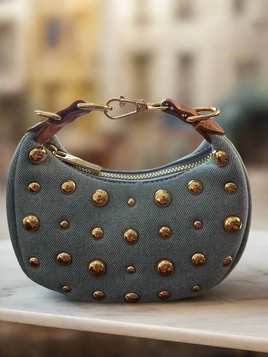 Blue denim handbag with gold studs on a white background