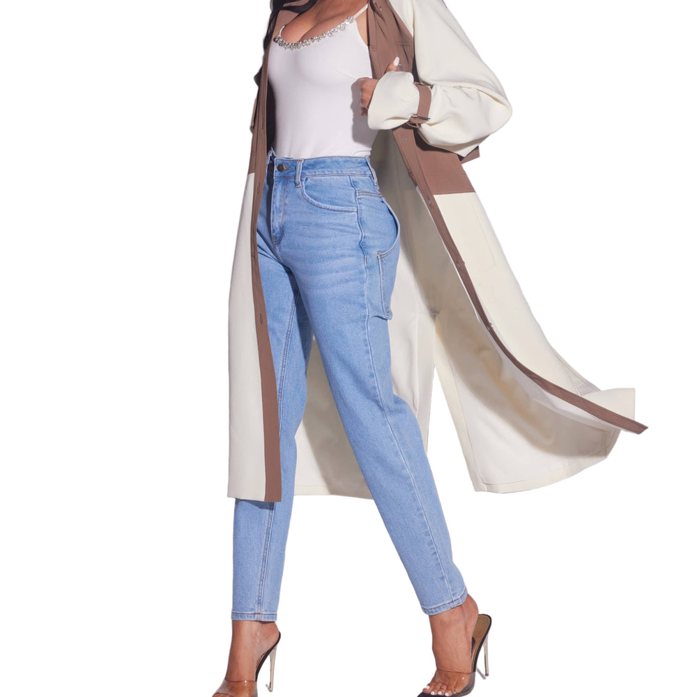 Woman wearing a long beige coat, white top, and blue jeans on a light gray background