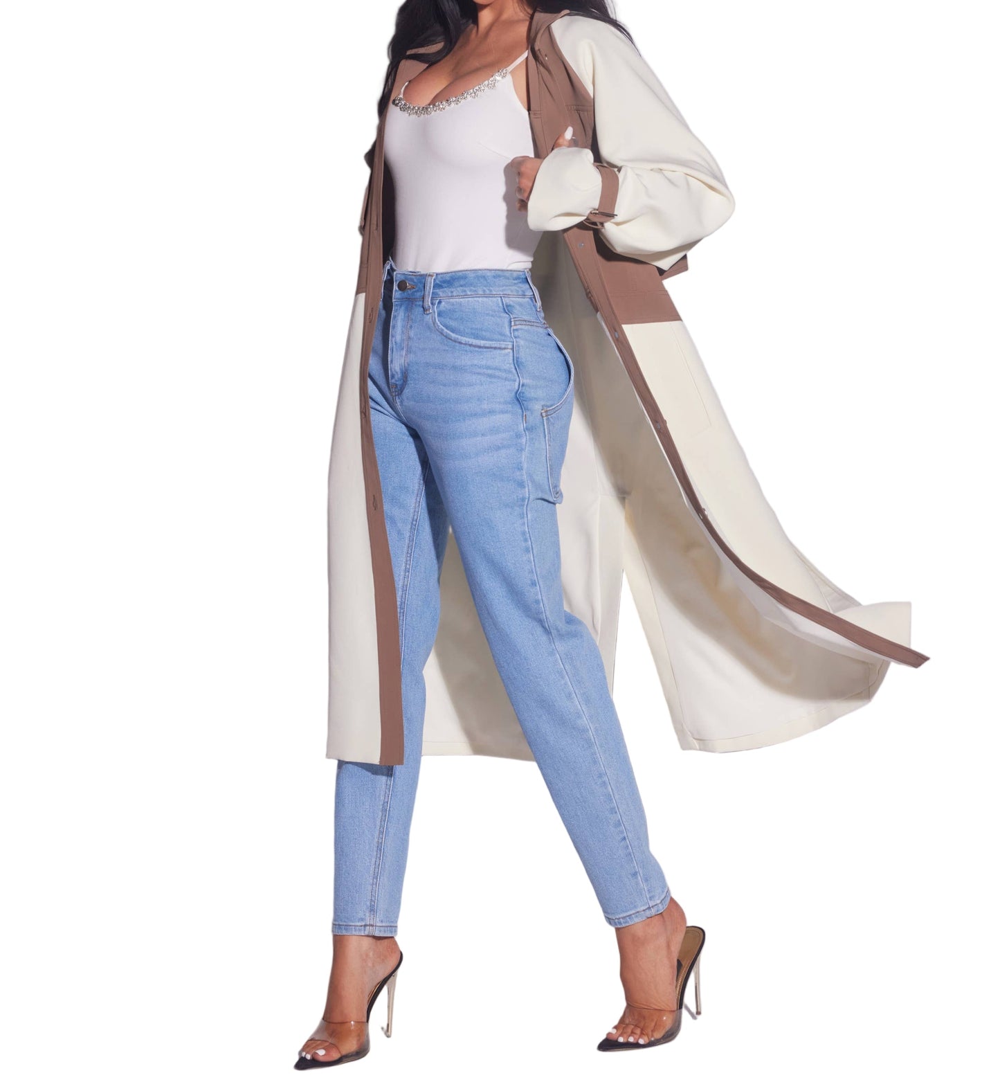 Woman wearing a long beige coat, white top, and blue jeans on a light gray background