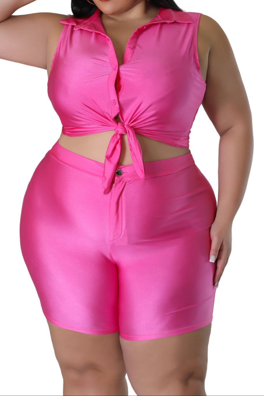 Woman wearing a bright pink outfit with a tied top and shorts on a plain background
